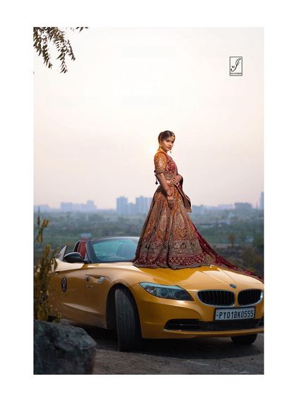 This wide shot captures the entire scene, blending the luxury of the car and the elegance of the traditional Indian attire with the natural landscape.