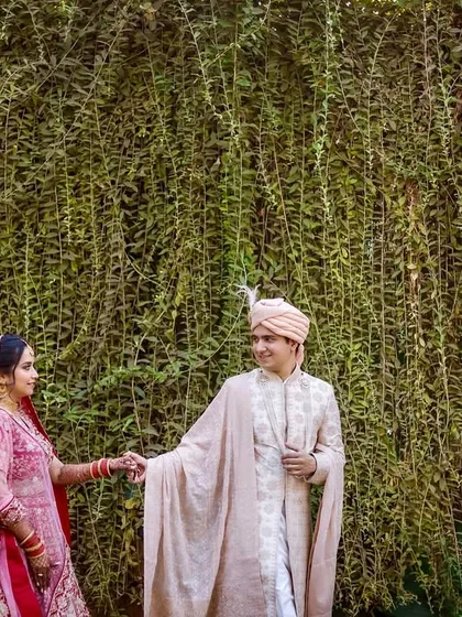 A wide shot of the couple holding hands against a stunning wall of green ivy. The groom leads his bride, creating a beautiful, cinematic feel for this wedding day portrait.