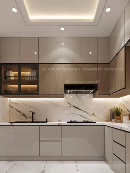 A luxurious L-shaped kitchen combining beige and wood-finish cabinets with a stunning marble backsplash. The design includes a glass-fronted cabinet and a false ceiling with integrated lighting.