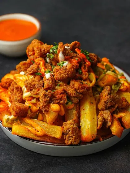 A bowl of loaded fries topped with savory minced meat and a creamy sauce, served with a side of spicy dip. The dark, contrasting background makes this an ultimate comfort food shot.