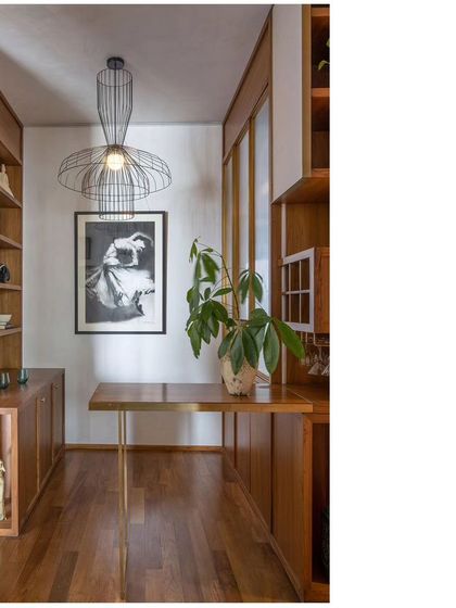 A cozy nook designed as a home bar and reading corner. The space is defined by custom teak cabinetry and a sculptural pendant light.