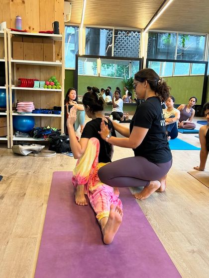An instructor provides a stabilizing adjustment in a seated spinal twist. This helps the student ground through their sit bones while rotating from the thoracic spine, a key detail for a healthy and effective twist.