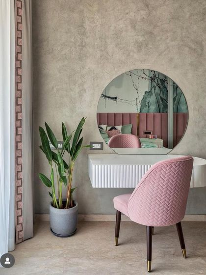 A minimal dressing unit in a bedroom, featuring a floating white console, a round mirror, and a plush pink chair. The textured grey wall provides a calm and sophisticated backdrop.