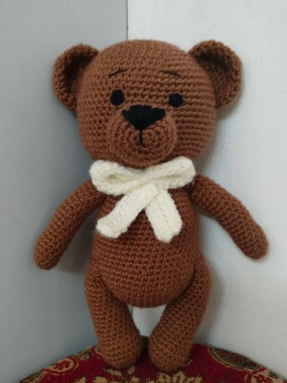 A classic handmade teddy bear with a cream-colored bow. This brown bear is soft, cuddly, and a timeless friend for any child.