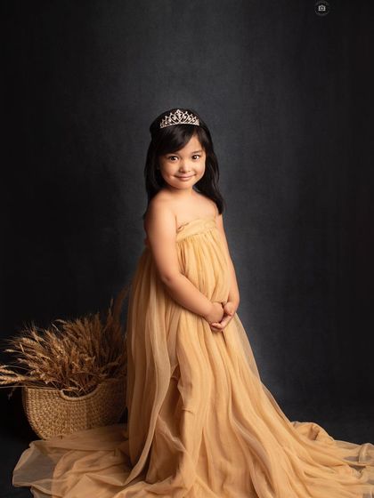 A beautiful, classic portrait of a five-year-old princess. Her sweet smile and the elegant golden gown shine against the dark, dramatic background.