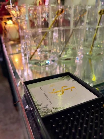 A custom coaster with the event hashtag #sanjtookthedive, placed neatly on the bar mat. It's a functional detail that also encourages social sharing.