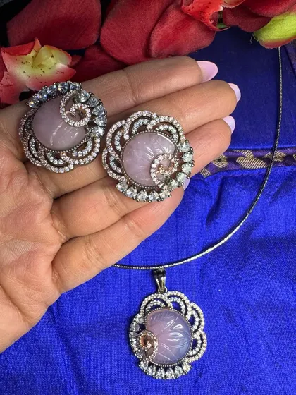 For those who love subtle elegance, this lilac-pink pendant set is a perfect choice. The soft color of the carved stone is beautifully accented by the two-tone setting and sparkling diamond-like stones.