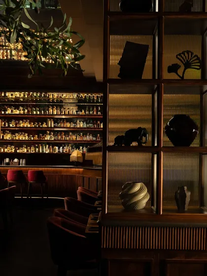 A detail of the shelving, filled with curated artifacts, set against the backdrop of the brilliantly lit bar. This composition creates a dialogue between intimate objects and the grand scale of the space.
