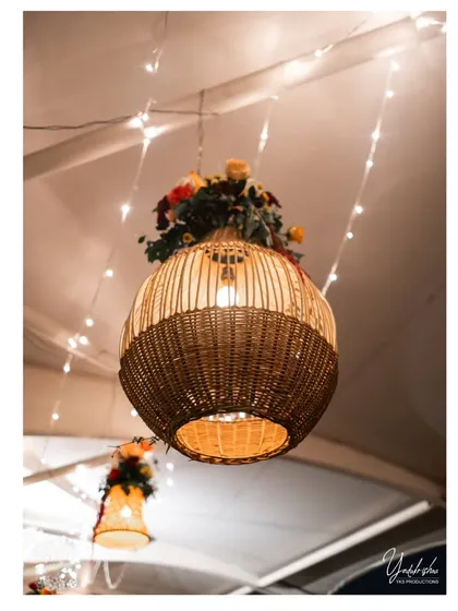 A close-up of a large wicker pendant lamp decorated with flowers, a key element in the boho-themed reception decor.