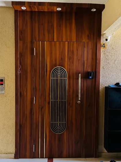 A full entrance design featuring a wooden safety door with vertical brass inlays and a central grill. The door is equipped with a smart lock for keyless entry.