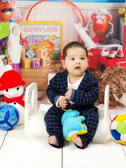 Another angle of the baby boy in his plaid suit, surrounded by a colorful explosion of toys.
