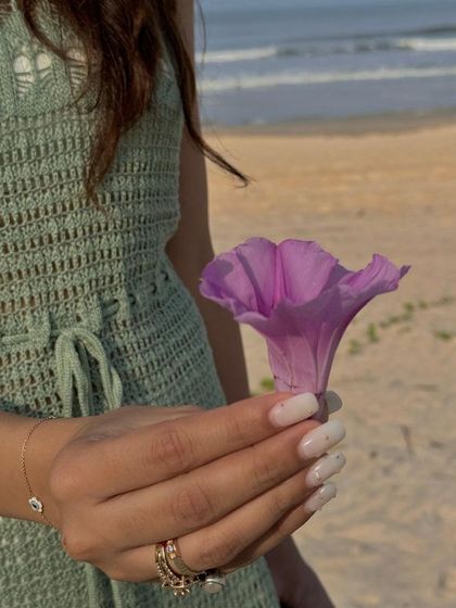 A beautiful shot of a white manicure at the beach, holding a flower.