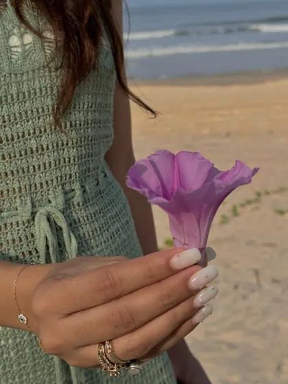 A beautiful shot of a white manicure at the beach, holding a flower.