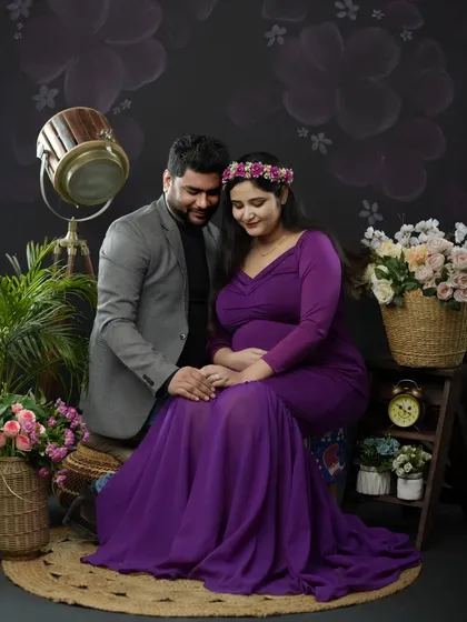 A formal and elegant studio portrait. The couple, dressed in complementary colors, shares a quiet moment in a beautifully arranged setting with floral and vintage props.
