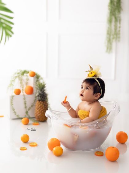 A whimsical shot of the baby looking up during her orange-themed fruit bath. The composition creates a sense of wonder and fun.