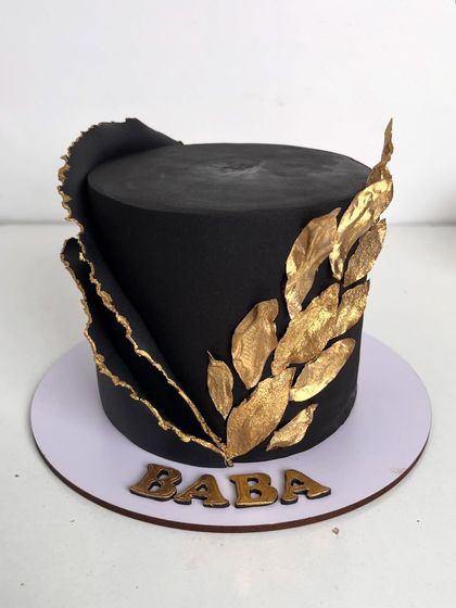 Bold, classy, and timeless. This single-tier cake features a sleek black fondant finish, accented with a dramatic black sail and a spray of hand-painted golden leaves, personalized for "Baba."