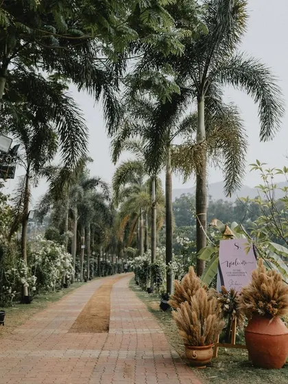 The pathway to a lakeside anniversary party, marked by a welcome sign and arrangements of pampas grass, setting a natural and elegant tone.