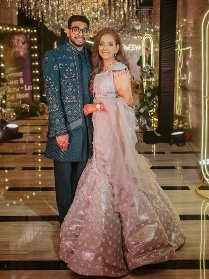 A full-length shot of the couple, showcasing her complete sangeet look. The makeup, hair, and outfit all come together to create a perfectly coordinated and glamorous appearance.