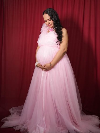 A full-length view of the one-shoulder pink maternity gown. Its long, flowing design is very flattering and creates a soft, elegant silhouette.