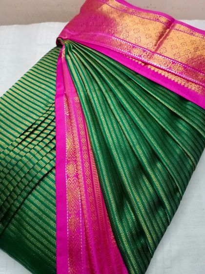 A rich green silk saree with a pink border. The pleats are crisp and the saree is ready to be draped in under five minutes.
