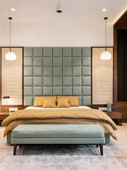 A serene and symmetrical master bedroom design. The large, quilted sage-green headboard is the centerpiece, flanked by elegant pendant lights that provide warm reading light.
