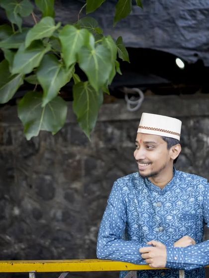 A candid portrait of the groom, smiling as he leans against a railing in a natural, outdoor setting.