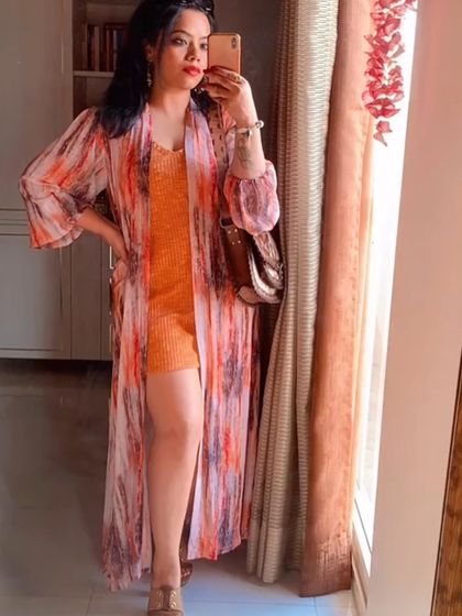 A mirror selfie of the vibrant orange and printed shrug outfit.