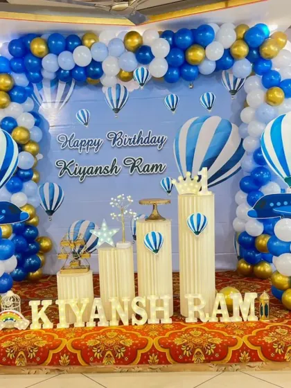 An "Up, Up and Away" hot air balloon themed birthday. The blue sky backdrop is framed by a blue, white, and gold balloon arch, with airplane and hot air balloon cutouts adding to the travel theme.
