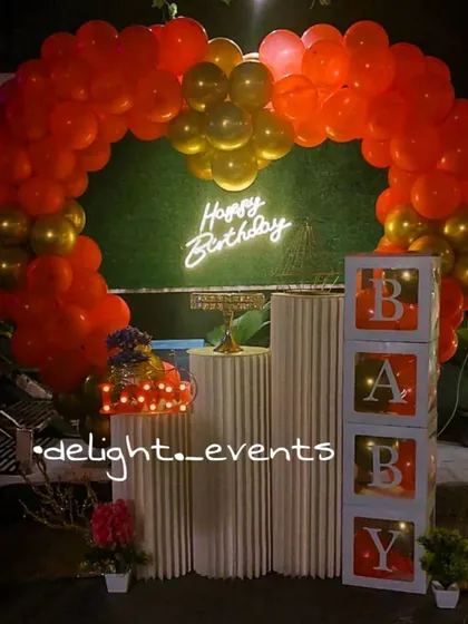 This vibrant setup combines a lush red and gold balloon arch with a "Happy Birthday" neon sign, creating a perfect photo booth. We also included 'BABY' display blocks and tiered pedestals for the cake and other decor elements.