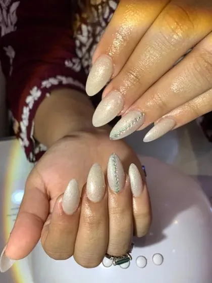 A glamorous set of stiletto nails with a shimmery nude base and a single line of crystals on the accent nails.