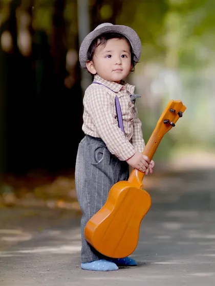 A toddler stands on a path holding a small guitar, a great prop for adding a playful element to outdoor kids' photography.