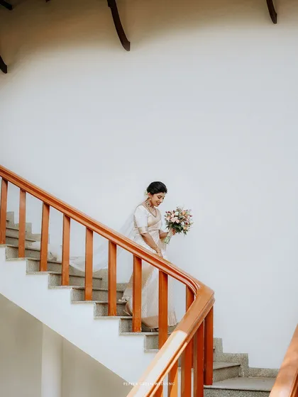 The bride descending a spiral staircase, a graceful and elegant shot that highlights the movement of her saree and veil.
