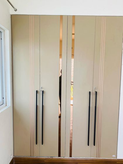 The exterior of a four-door wardrobe in a beige finish, featuring long black handles and elegant mirror strips for a modern look.