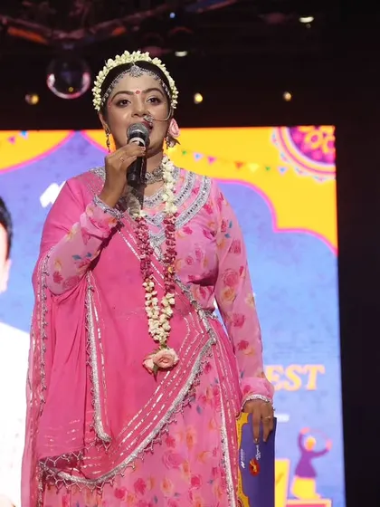 A powerful shot of me hosting as Radha, holding my notes and commanding the stage.