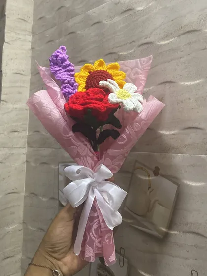 A pretty and vibrant bouquet featuring a mix of a red rose, a sunflower, a daisy, and lavender, all wrapped in heart-patterned pink paper. It’s a little bit of everything in one colorful bunch.