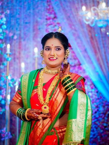 A candid bridal portrait where the bride adjusts her traditional gold necklace. Her slight smile and the vibrant colors of her saree make for a beautiful, natural shot.
