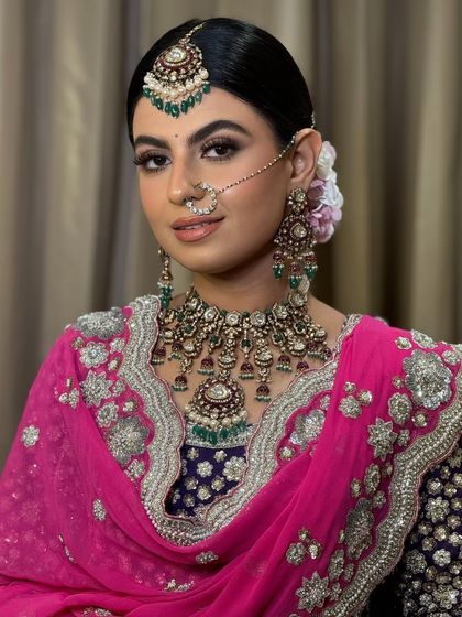 A Sikh bride ready for her Anand Karaj ceremony. Her hair is styled in a neat, low bun, providing a perfect base for her dupatta and the intricate passa and maang tikka.