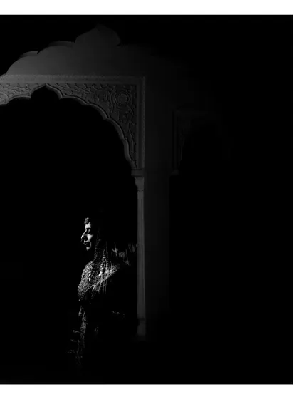 A moody black and white portrait of the bride, framed by a dark archway. This artistic use of negative space and light creates a striking and contemplative image.