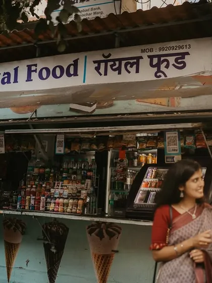 A wider view of the chai stall, placing the couple's intimate moment within the context of the bustling city. This environmental portrait tells a story about who they are and the places they share.
