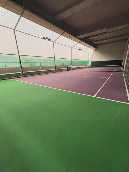 A wide shot of my versatile indoor court, showing the striking purple and green surface used for tennis and pickleball. The high ceiling and enclosed space make it perfect for all-weather play.