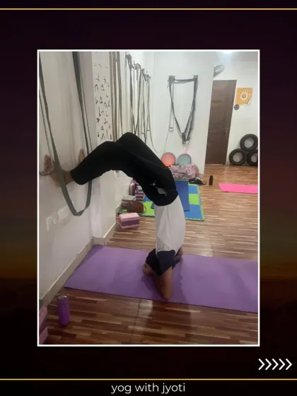 A student works on Vrishchik Asana (Scorpion Pose) using the wall for support, building strength and flexibility.
