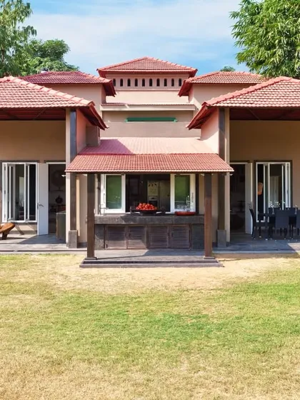 The front facade of the Aishbagh cottage, showcasing its symmetrical design and layered, sloped roofs with terracotta tiles. The architecture is designed to feel organic and rooted in its natural environment.
