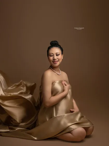 Wrapped in liquid gold. This stunning portrait uses flowing satin fabric to create a regal and elegant look, highlighting the beauty and serenity of this special time against a warm, earthy backdrop.