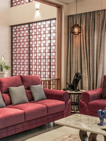 The living area features deep red sofas that provide a bold splash of color against the neutral backdrop, with a jali screen filtering light from the courtyard.