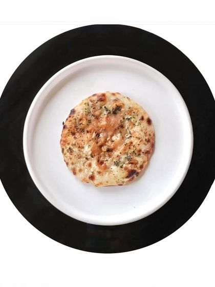 A simple, perfectly baked naan, presented on a white plate against a black background. Your journey at Indian Accent is incomplete without our breads.