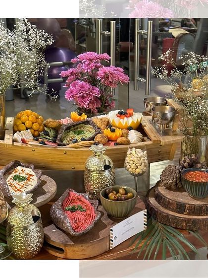 A boat-shaped platter adds a unique touch to this grazing display, filled with an assortment of dips, nuts, and crackers, surrounded by fresh flowers.