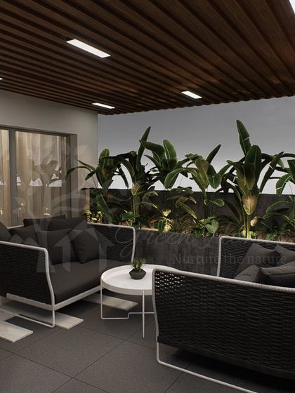 The main seating area of the Ashok Vihar terrace, featuring modern wicker furniture set against a backdrop of lush planters. The wood-paneled ceiling adds warmth to the covered space.
