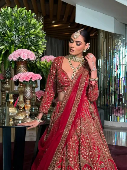 A regal pose by a floral arrangement. The styling of this red lehenga is designed to feel grand and luxurious in any setting.
