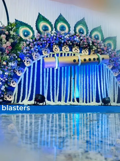 A full view of my popular Krishna-themed naming ceremony decor. The setup features a custom-built backdrop with a large flute, peacock feather details made from natural materials, and a cascade of white tuberose garlands, creating a divine and vibrant setting for the celebration.