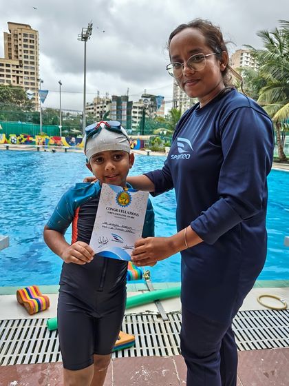 A female coach congratulates a young male student on his progress, presenting him with a certificate by the poolside.